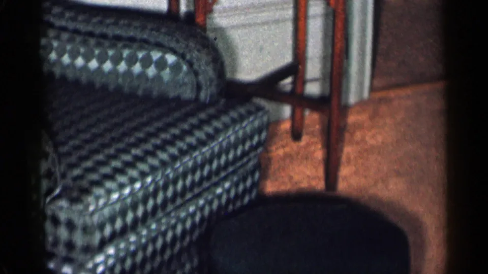 1955 New York City interior frame with the checkered armchair continuing across the pan and a dark ottoman in the foreground.