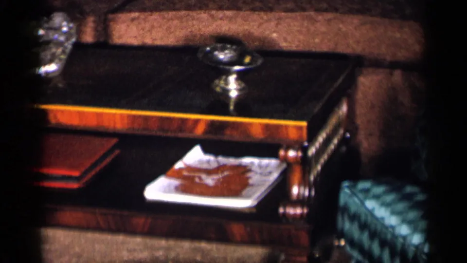 The camera settles on a dark wooden side table with a glass ashtray, decorative dish, and nearby upholstered furniture.