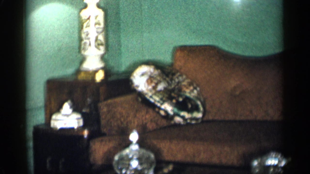 Brown sofa against a green wall with a ceramic lamp, side table, pillow, and glass containers.