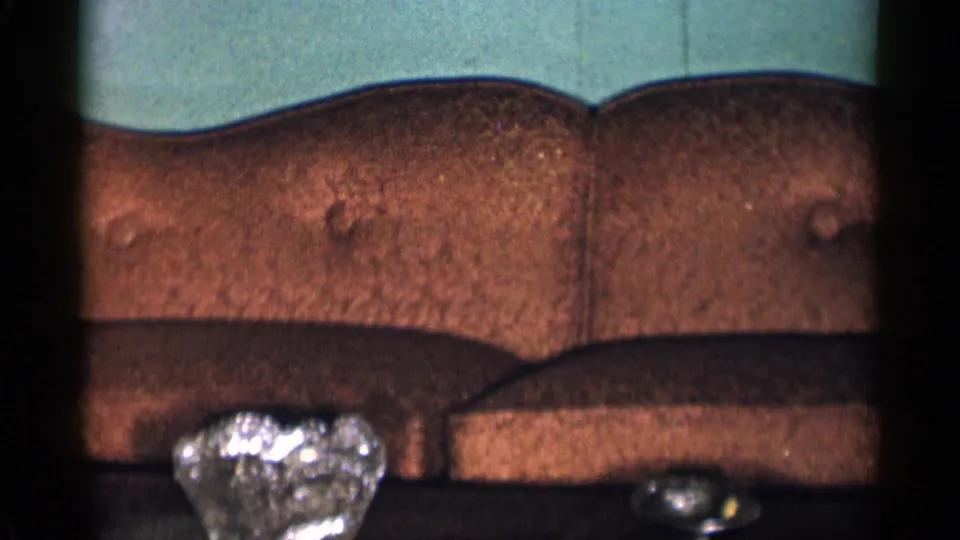 1955 New York City living room frame centered on the brown tufted sofa, green wall, and partially visible glass table objects.