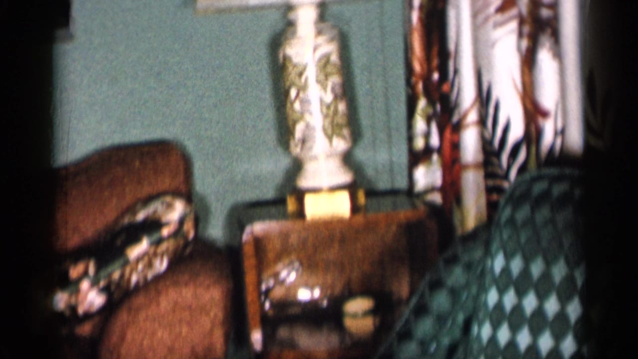 Living room corner with brown armchair, patterned pillow, side table, lamp, and floral curtains.