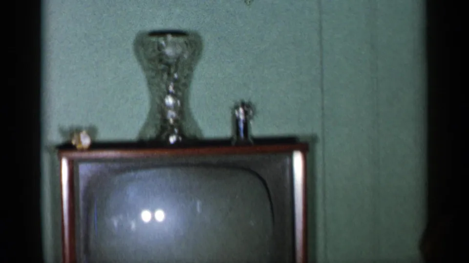A mid-century wood-cabinet television stands in a New York City interior with a glass vase and small display items above it.
