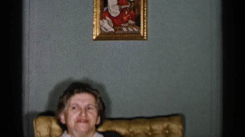 1955 New York City 8mm frame showing the woman partially low in the shot, with a small framed painting and pale green wall above her.