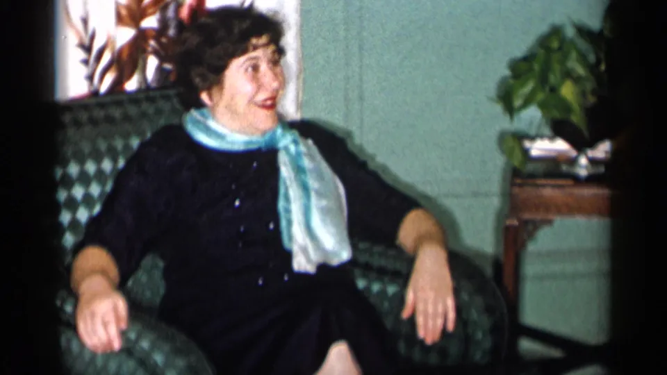 A 1955 home-movie frame shows the seated woman turning her face upward as if speaking to someone off camera.