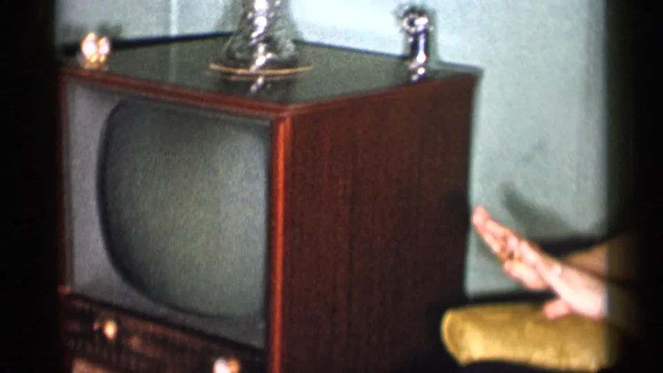 1955 New York City home interior showing a console television and a woman's hand gesturing near an upholstered chair.