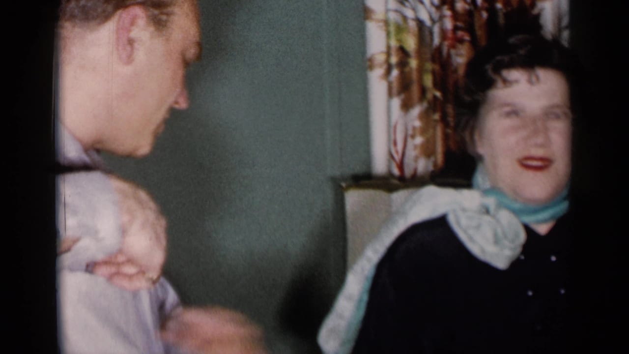 Man turns toward a seated woman near patterned curtains and a table lamp.