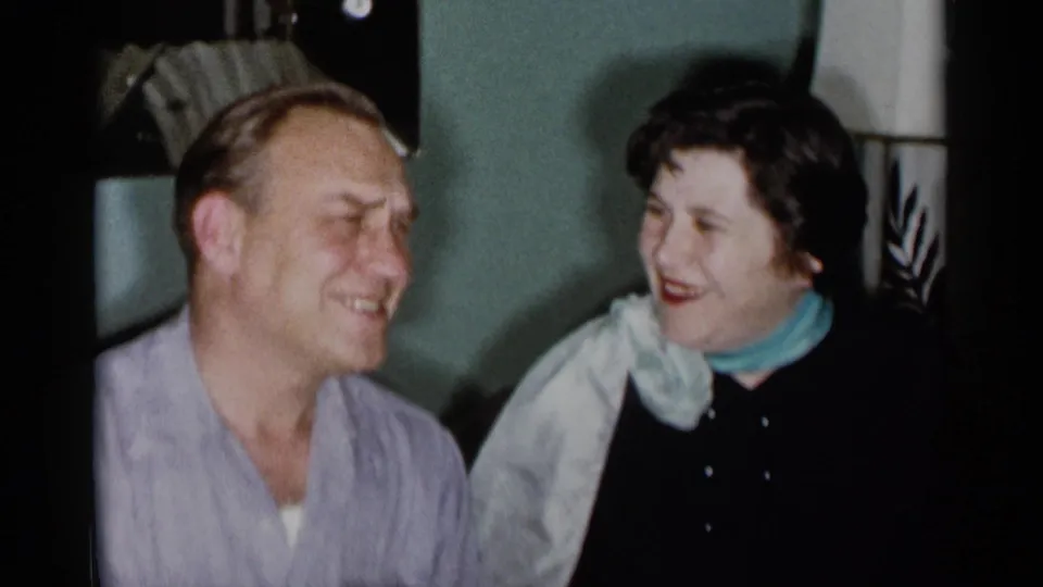 1955 New York City home-movie frame showing a man laughing beside a smiling woman in a dim living room.