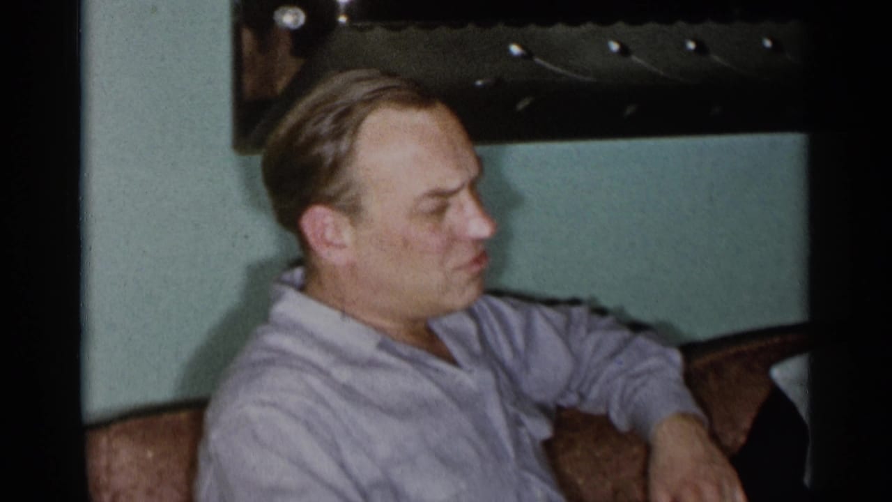 Man in a light shirt sits in profile beside upholstered seating indoors.