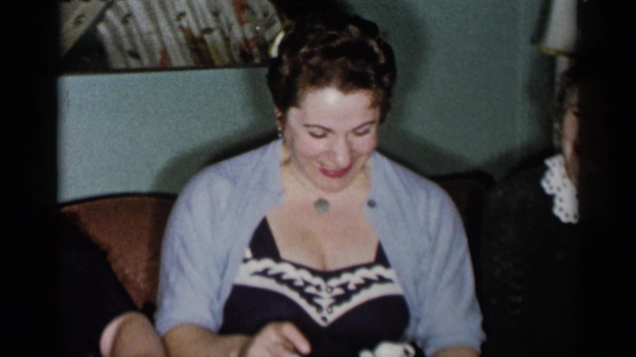 Woman in a light cardigan looks down while holding small white baby shoes.