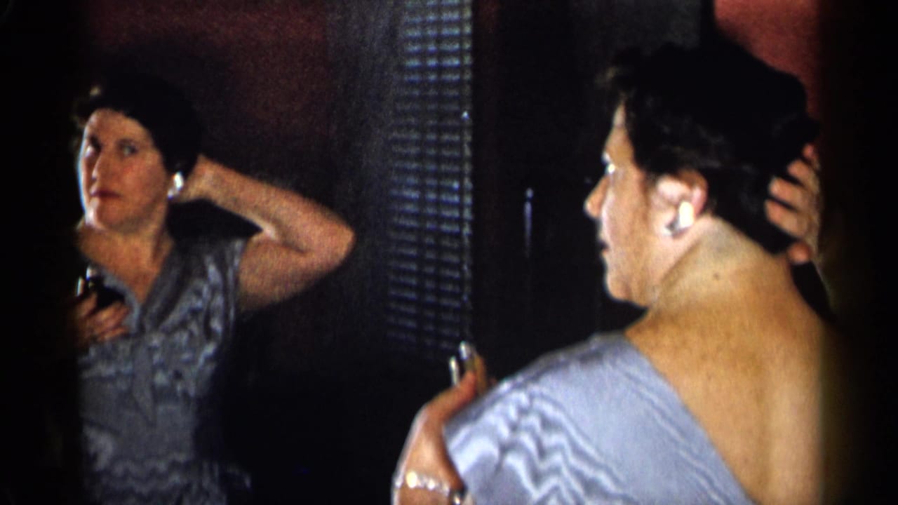 Woman adjusts her dark hair while holding a small cosmetic item near a mirror.