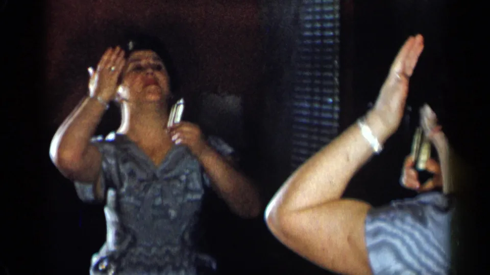 In the mirror view, the woman tilts her head back and touches her face during a 1950s home grooming moment.