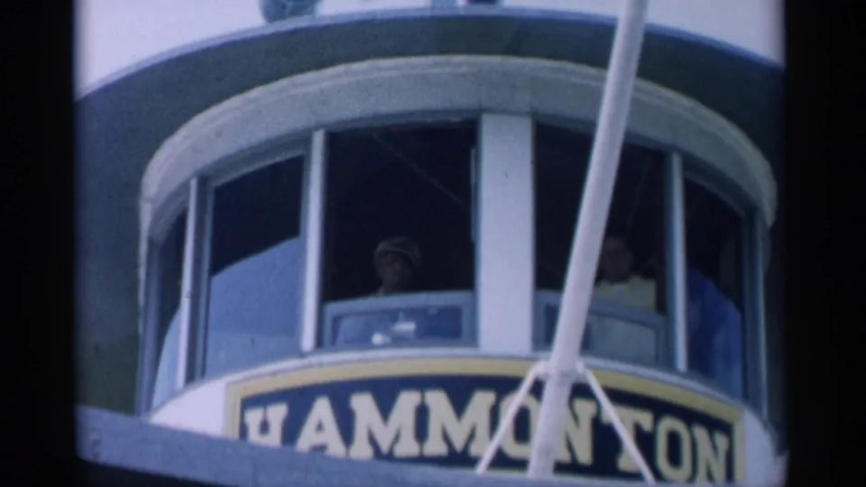 Uniformed captain appears inside the Cape Cod ferry pilothouse, with partial Hammonasset signage and rigging in the foreground.