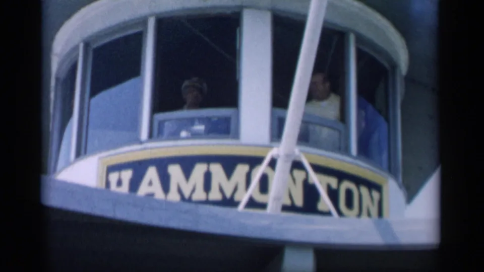 Cape Cod ferry pilothouse with the captain and nearby passengers visible behind windows and beside partial Hammonasset signage.