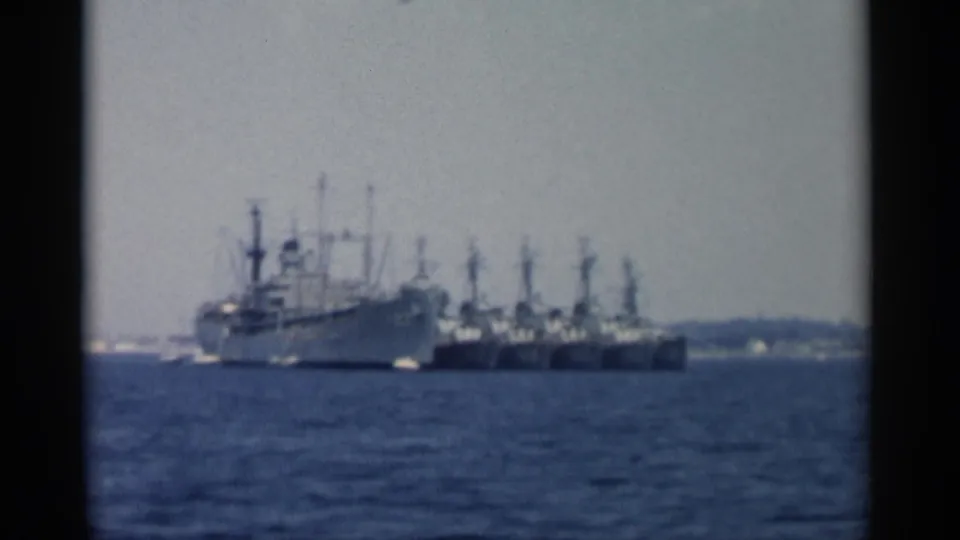 Soft 8mm view of a harbor fleet off Cape Cod in 1956, with a large gray vessel and smaller craft in the distance.