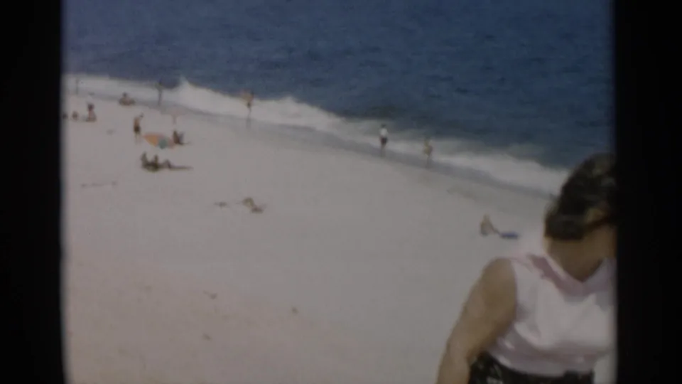 1956 Cape Cod beach scene with distant beachgoers near the surf and a woman in a light sleeveless top partly entering the frame.