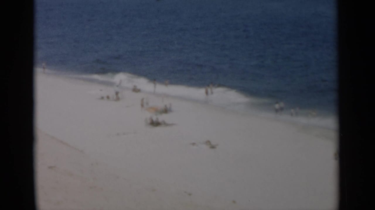 Wide beach view with scattered people on sand and small waves breaking along the shore.
