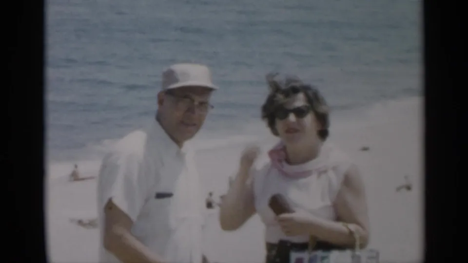 1956 Cape Cod home-movie frame showing a man in a white cap beside a woman in sunglasses on a bright beach.