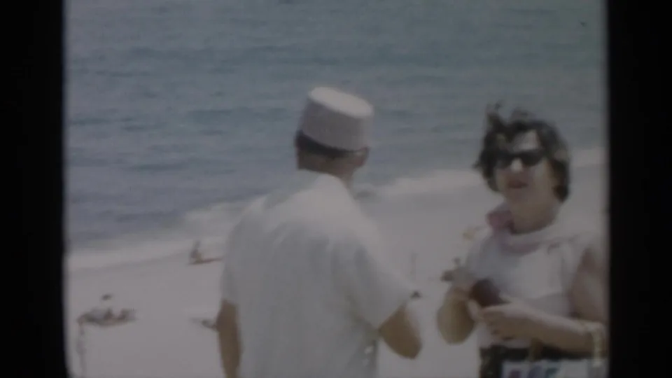 1956 Cape Cod home-movie frame showing the man from behind and the woman facing camera near the shoreline.