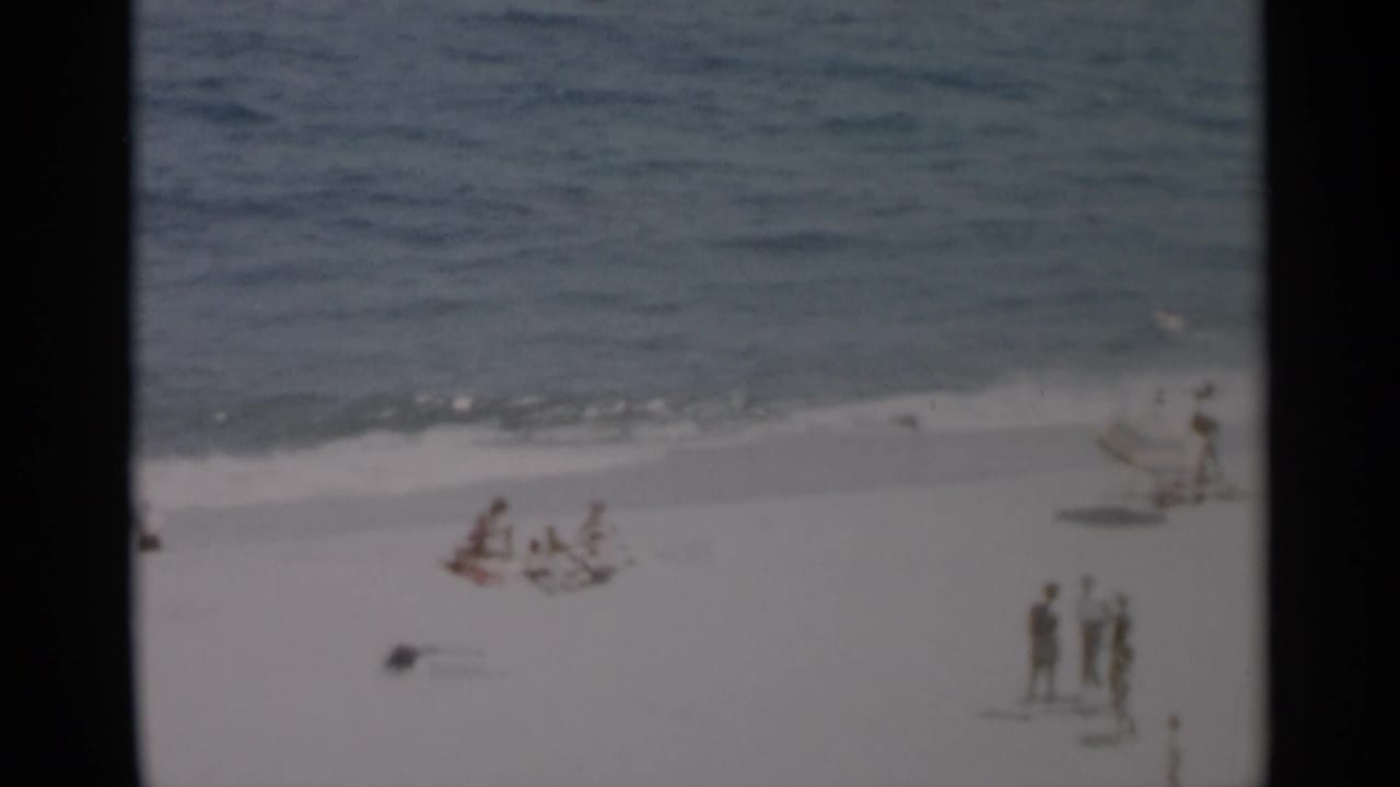 Wide beach view with people sitting and standing near the waterline.