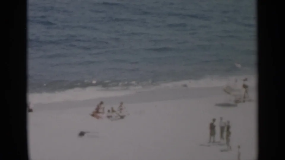 A wide Cape Cod beach view shows small groups of people on the sand beside calm surf in supplied 1956 footage.