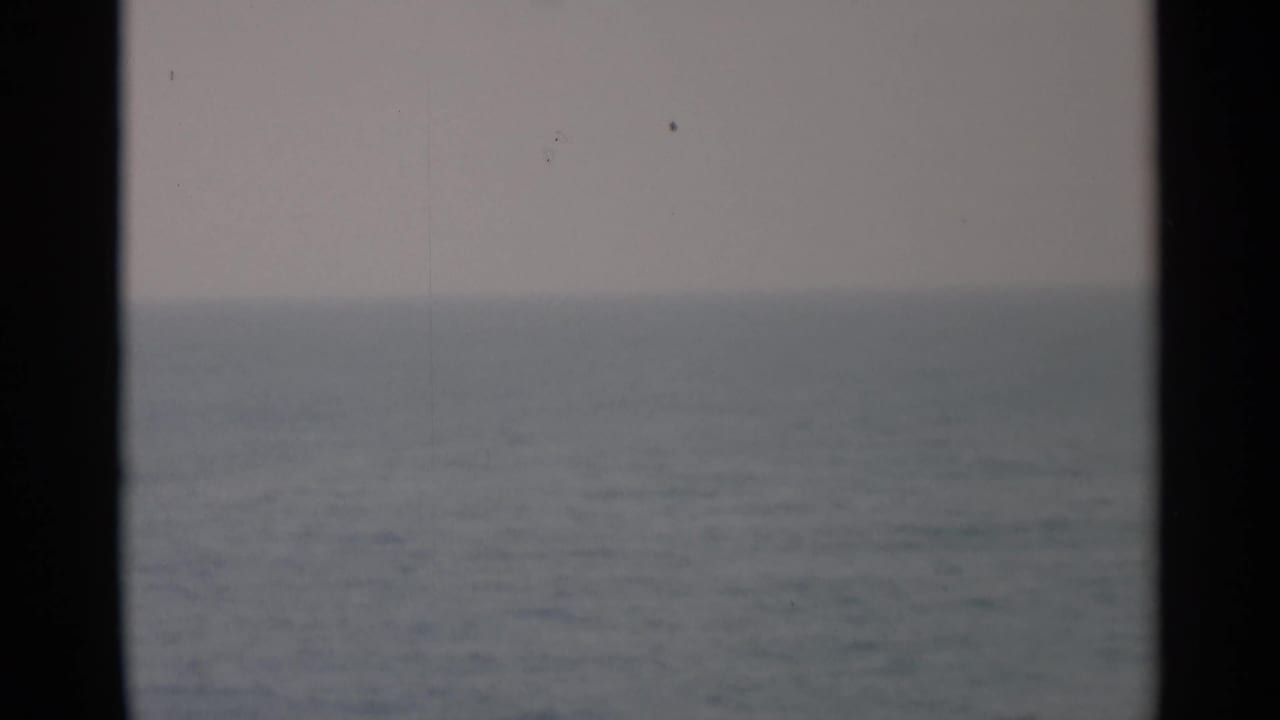 Hazy ocean horizon seen through dark vertical window or porthole edges.