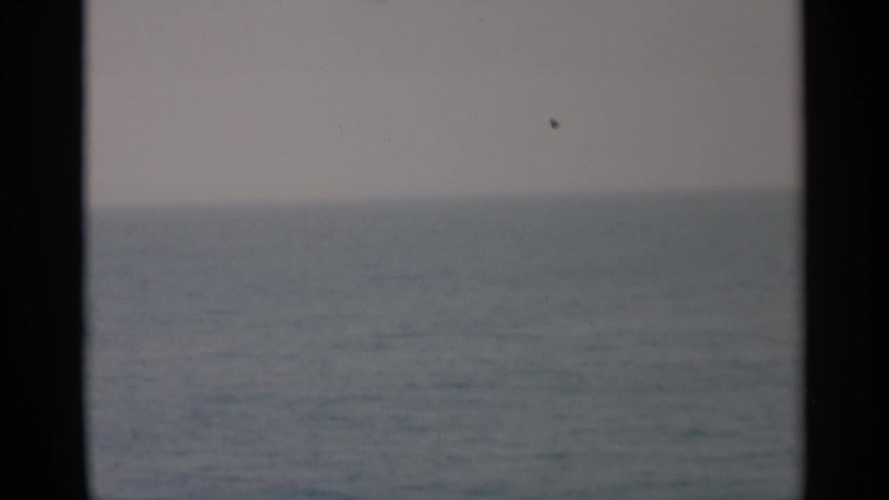 Soft 8mm view of open water off Cape Cod, divided by a dark vertical ship-window or porthole edge.