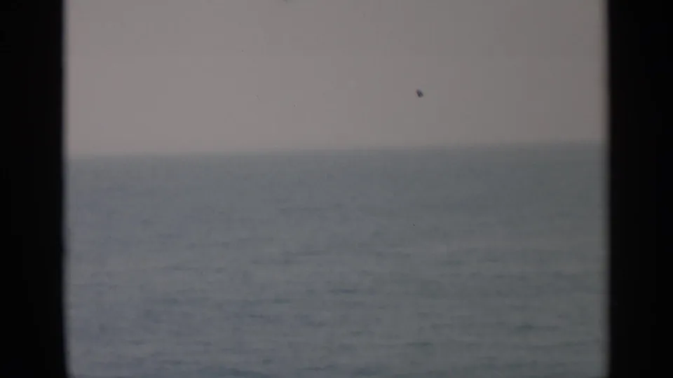 Soft 8mm view of open water off Cape Cod, divided by a dark vertical ship-window or porthole edge.