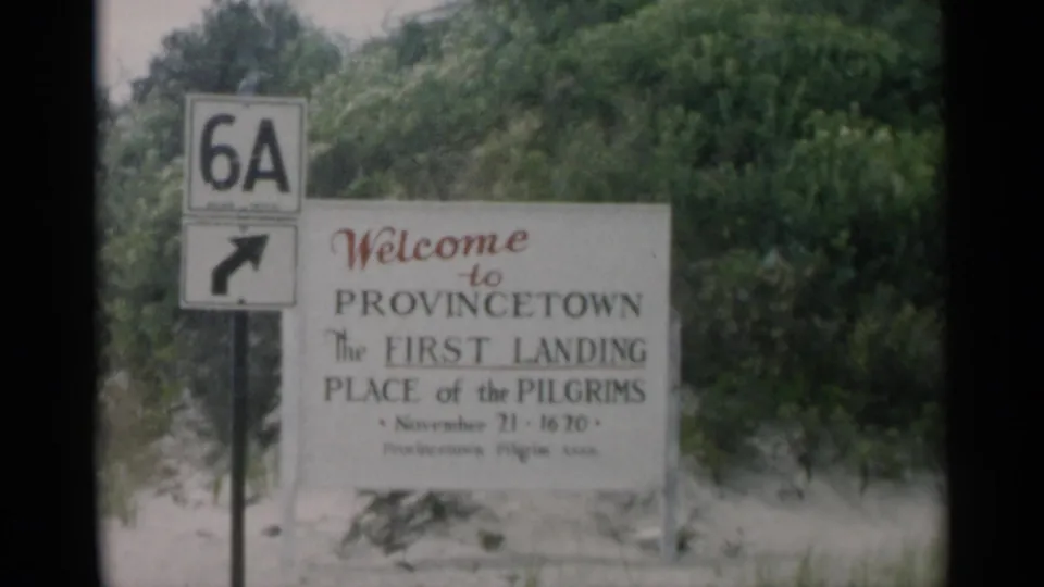 Provincetown, Massachusetts welcome sign beside a Route 6A marker, with sand and shrubs in the background.