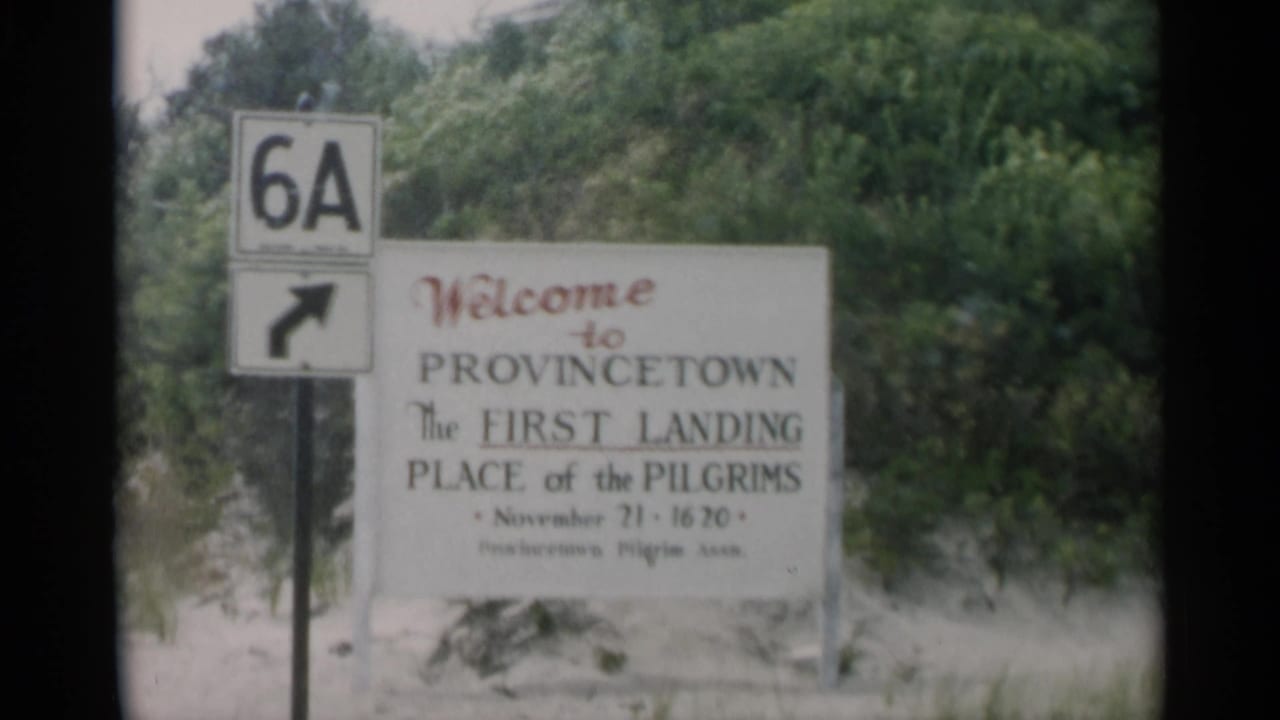 1956 Cape Cod home-movie frame showing a Provincetown welcome sign and Route 6A right-turn marker by shrubs and sandy ground.