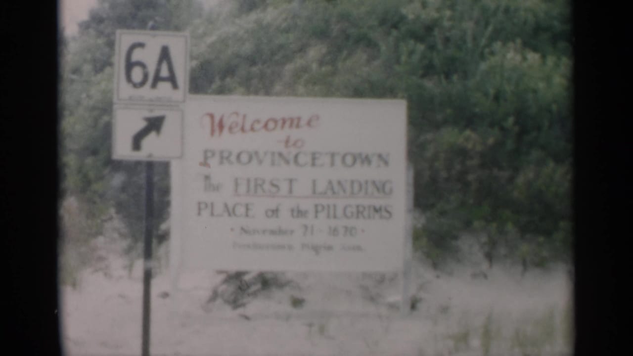 Provincetown welcome sign beside a Route 6A marker and roadside trees.