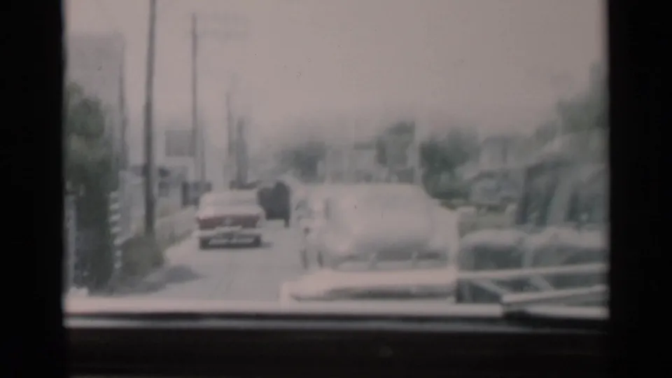 Soft 8mm view from a moving car on Cape Cod, showing vehicles, utility poles, and leafy roadside surroundings.