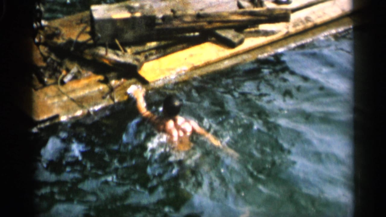 Man swimming beside a weathered wooden dock in choppy water.