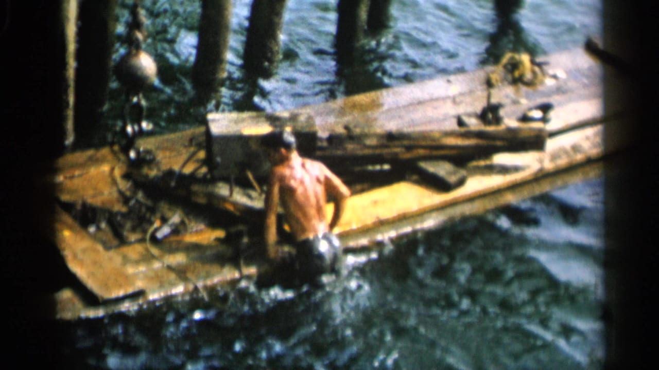 Swimmer approaches or climbs onto a weathered dock in 1956 Cape Cod footage.