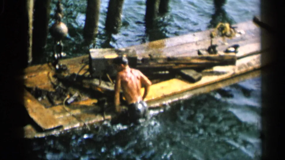 Swimmer approaches or climbs onto a weathered dock in 1956 Cape Cod footage.