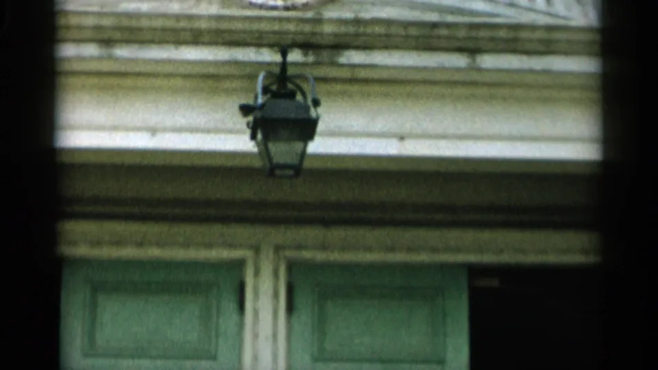 1956 Cape Cod frame showing a hanging lantern and weathered white trim above a green double door.