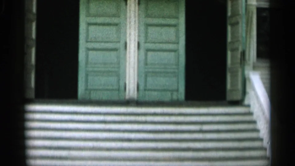 1956 Cape Cod home-movie frame with green doors at the top of white porch steps and deep shadows on both sides.