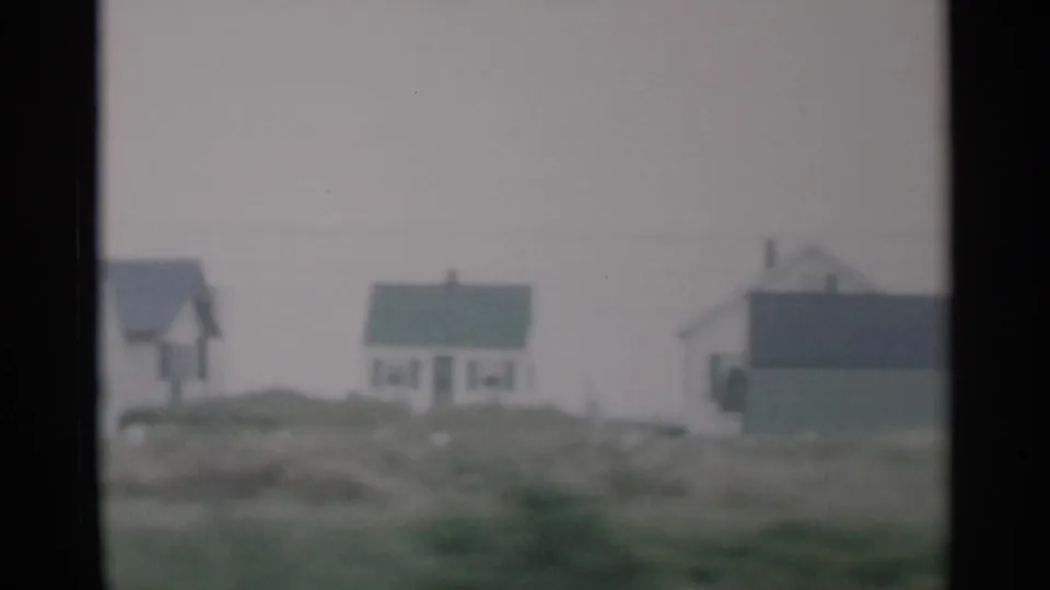 1956 Cape Cod frame showing small white houses, a green-sided building, low dunes, and a cloudy pale sky.