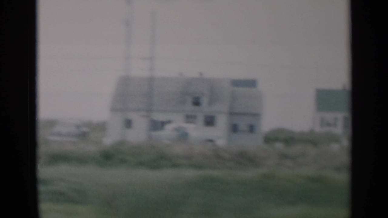 1956 Cape Cod home-movie frame showing small light-colored houses behind coastal grass on an overcast day.