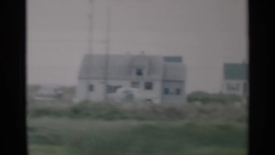 1956 Cape Cod home-movie frame showing small light-colored houses behind coastal grass on an overcast day.