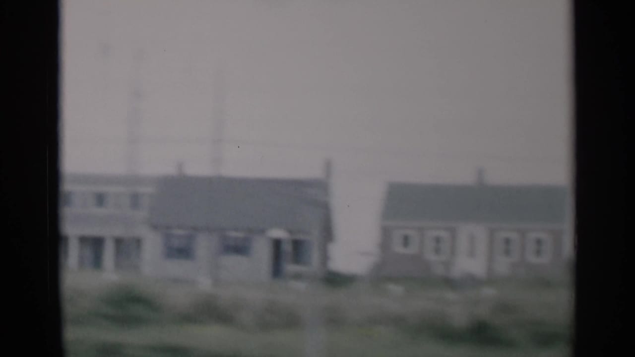 Cape Cod roadside houses appear across a grassy foreground in soft 1956 8mm color footage.