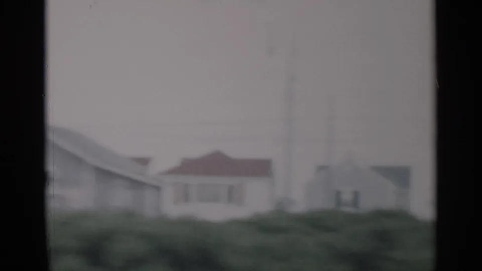 1956 Cape Cod frame showing a light house with red roof detail, tall antenna, and grassy foreground.