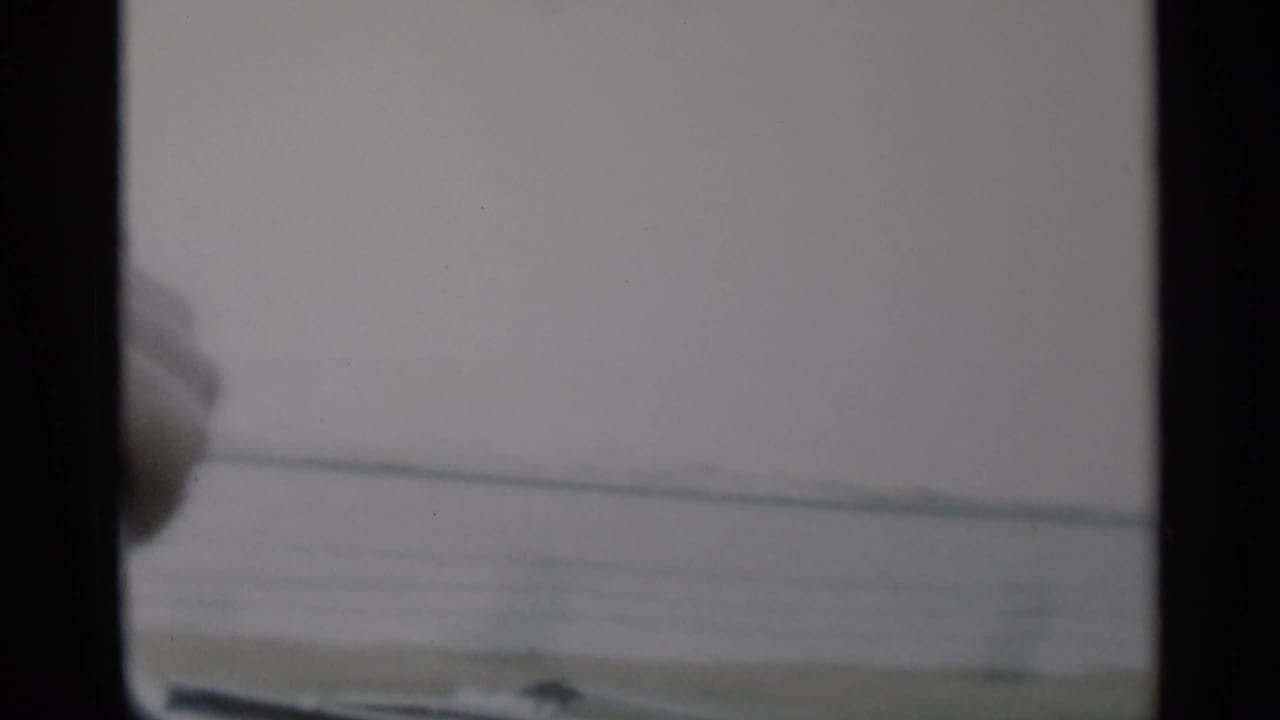 View through a car windshield toward hazy coastal water and a flat distant shoreline.
