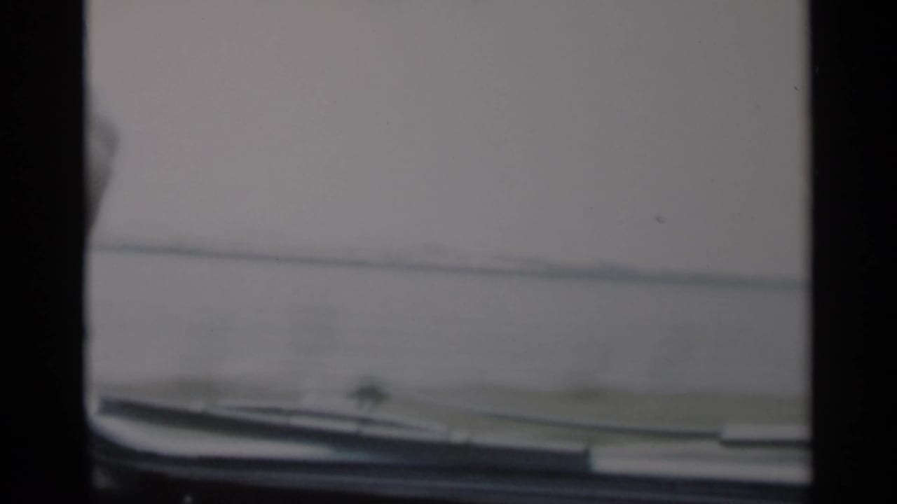 Car windshield and dashboard edge with coastal water and shoreline beyond.