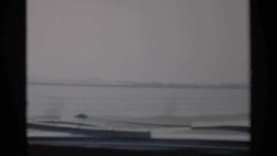 Inside-car Cape Cod view showing dark windshield framing, a dashboard edge, hazy water, and a flat distant shore.