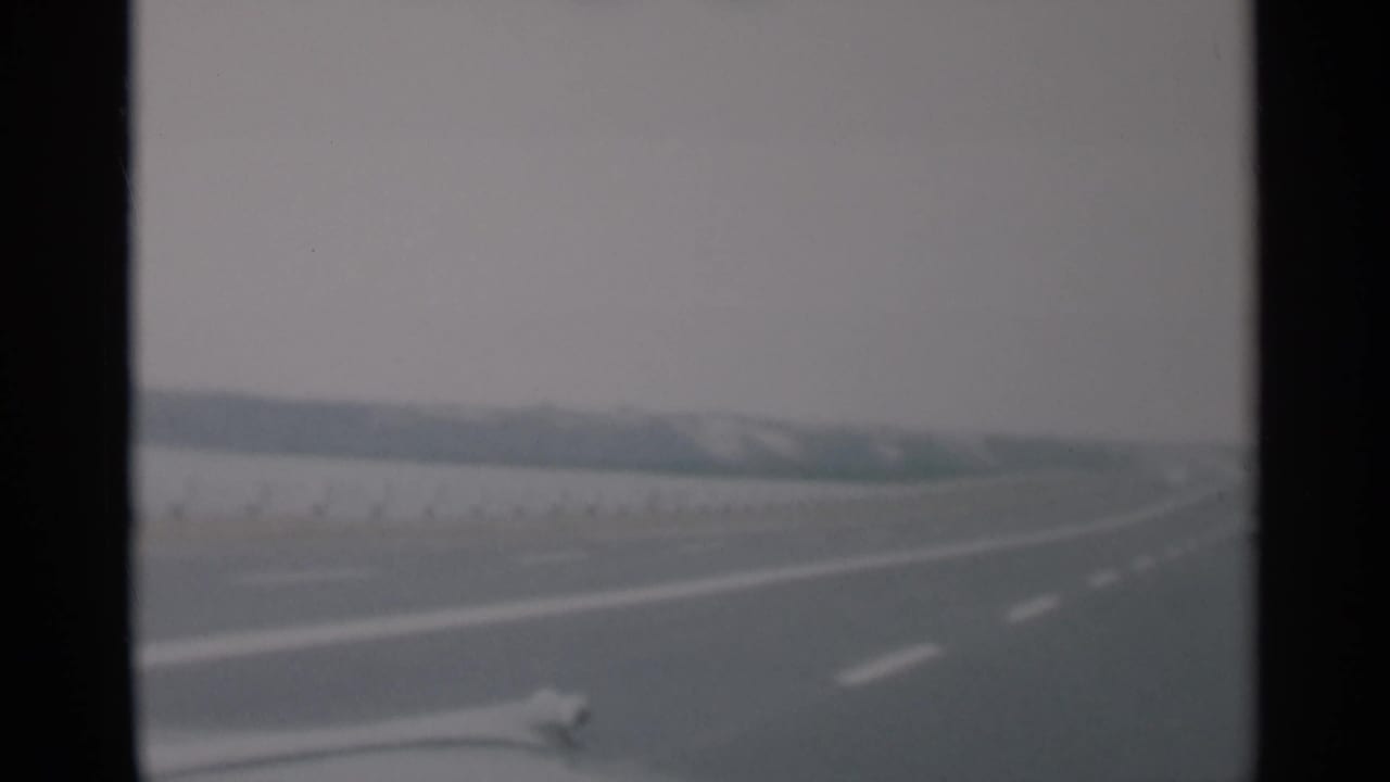 Open road seen from a moving vehicle, with white lane stripes and a distant low horizon.
