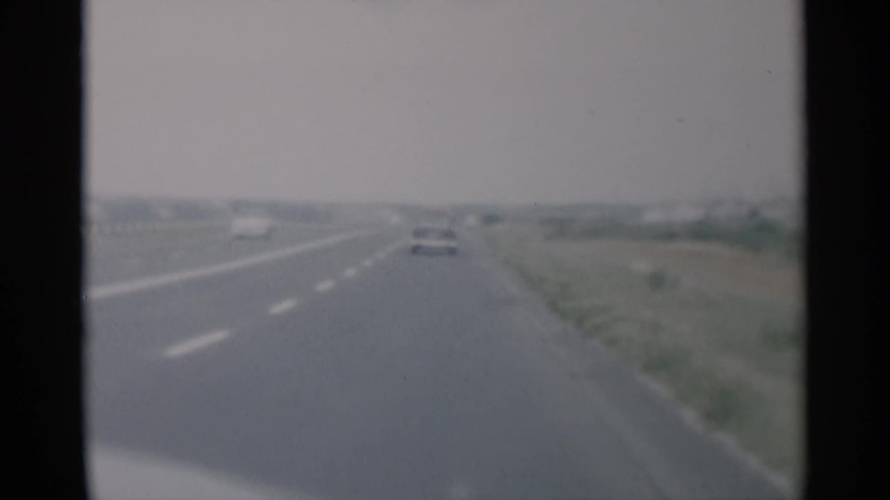 Forward view along a divided highway with distant cars under a gray sky.