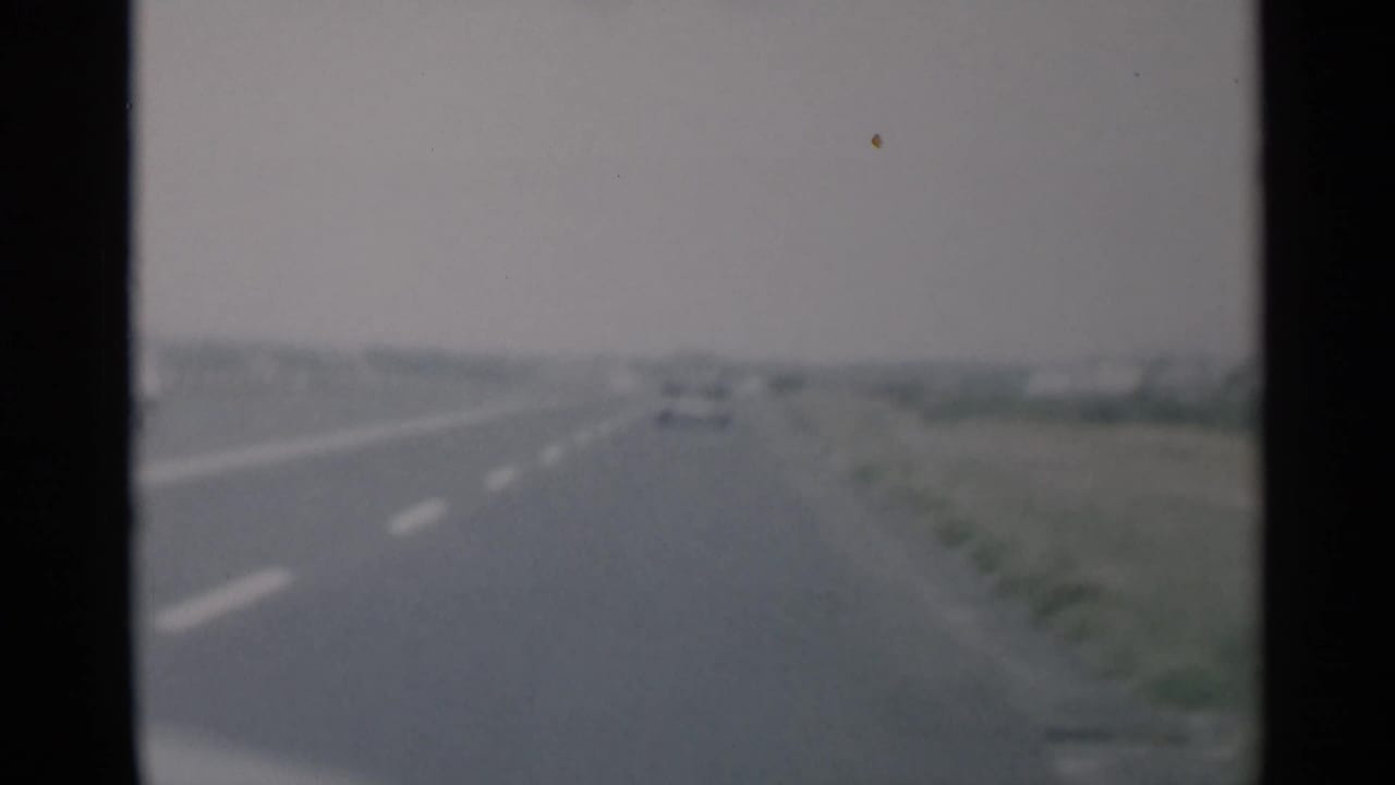 Blurred highway view with a car ahead and open roadside on both sides.