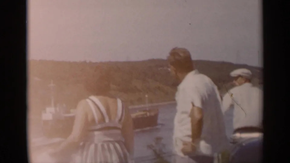 A faded 8mm frame shows the adults from behind as they continue watching the ship on the Cape Cod waterway.