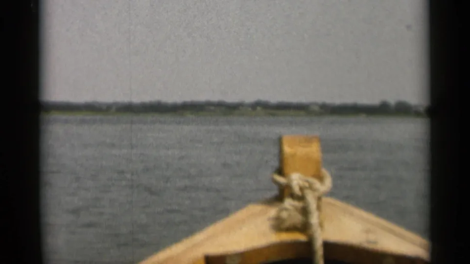 The wooden bow of the boat points over calm water toward a distant Cape Cod shoreline in 1956 home-movie footage.