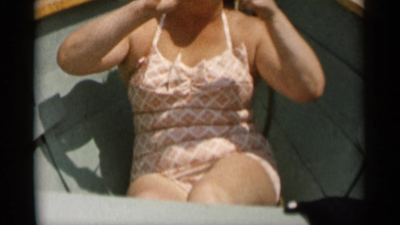 A close home-movie frame shows the woman seated inside the boat, with her patterned swimsuit and arms visible under bright sun.